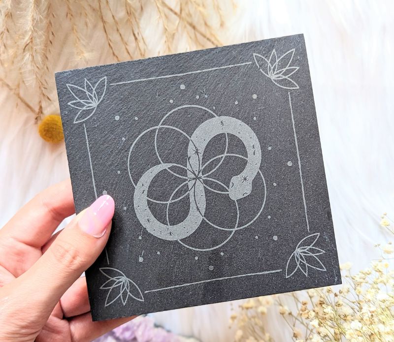 A woman&#39;s hand holding a black Goddess Provisions Infinite Magic Altar Tile. She has pink nails.